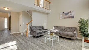 Un salon spacieux avec un canapé gris, une table basse en verre et un escalier menant à l’étage supérieur.