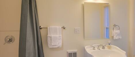 A bathroom with a shower curtain, a sink, a mirror, and two towels hanging on hooks.