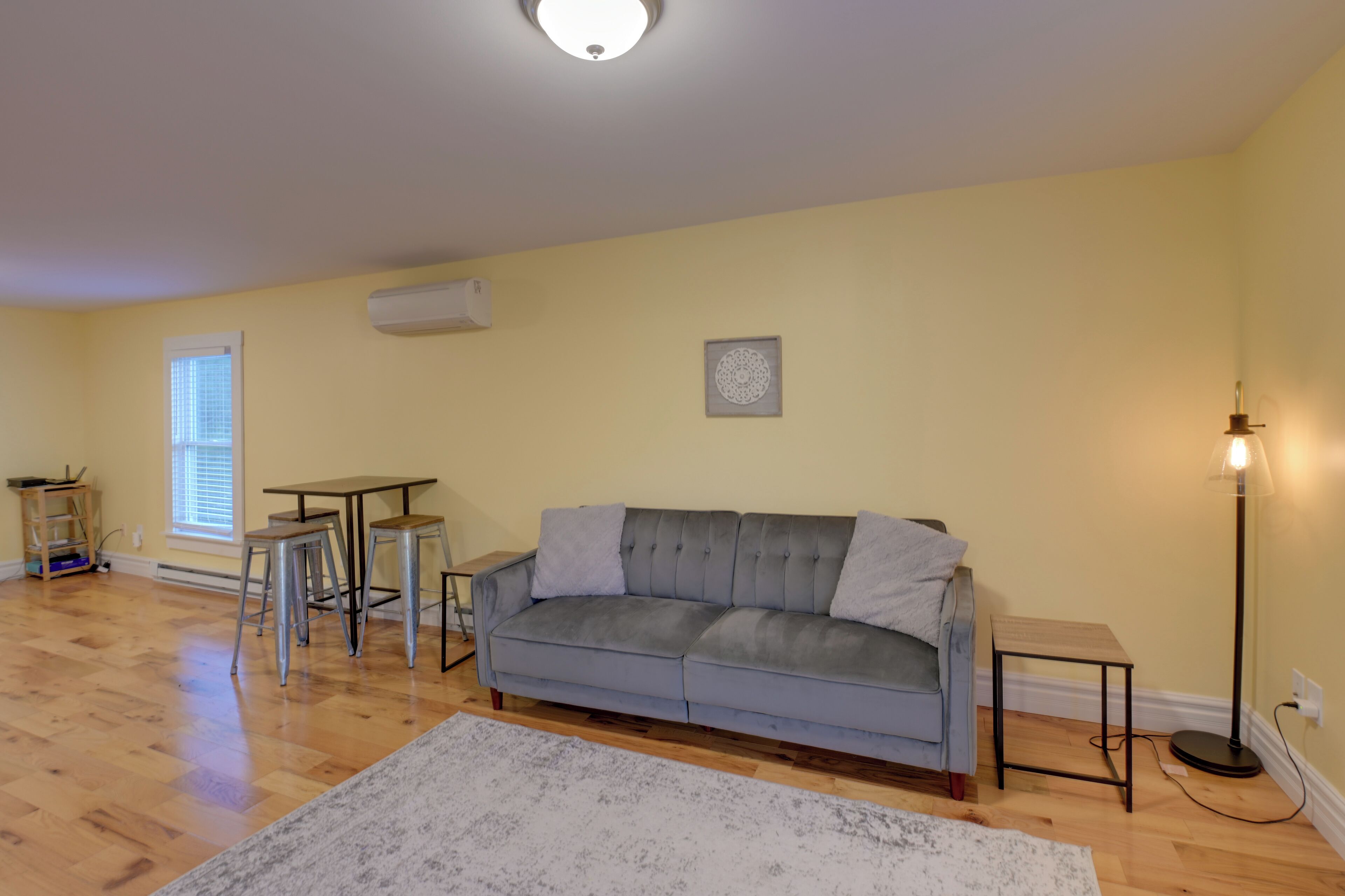 A living room with a grey sofa, two metal stools, a small wooden table, and a floor lamp.