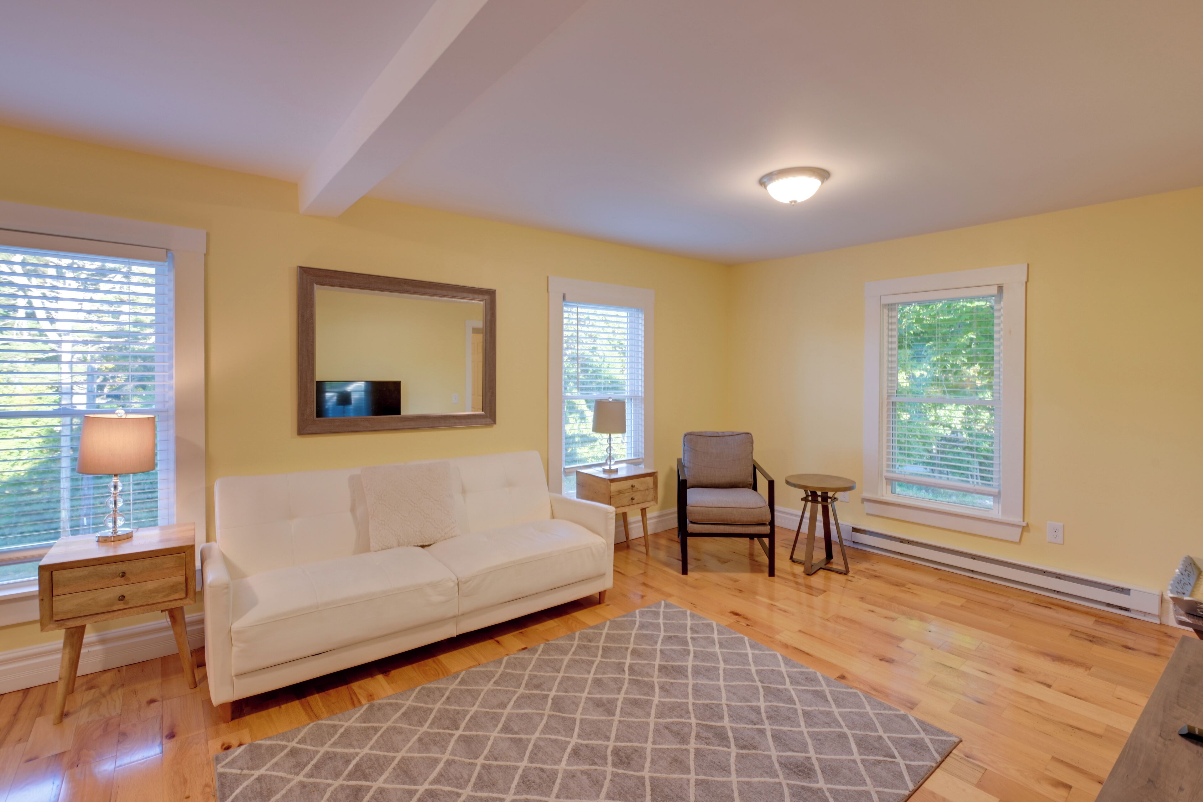 A living room with a white sofa, a gray rug, a small table with a lamp, and a chair.