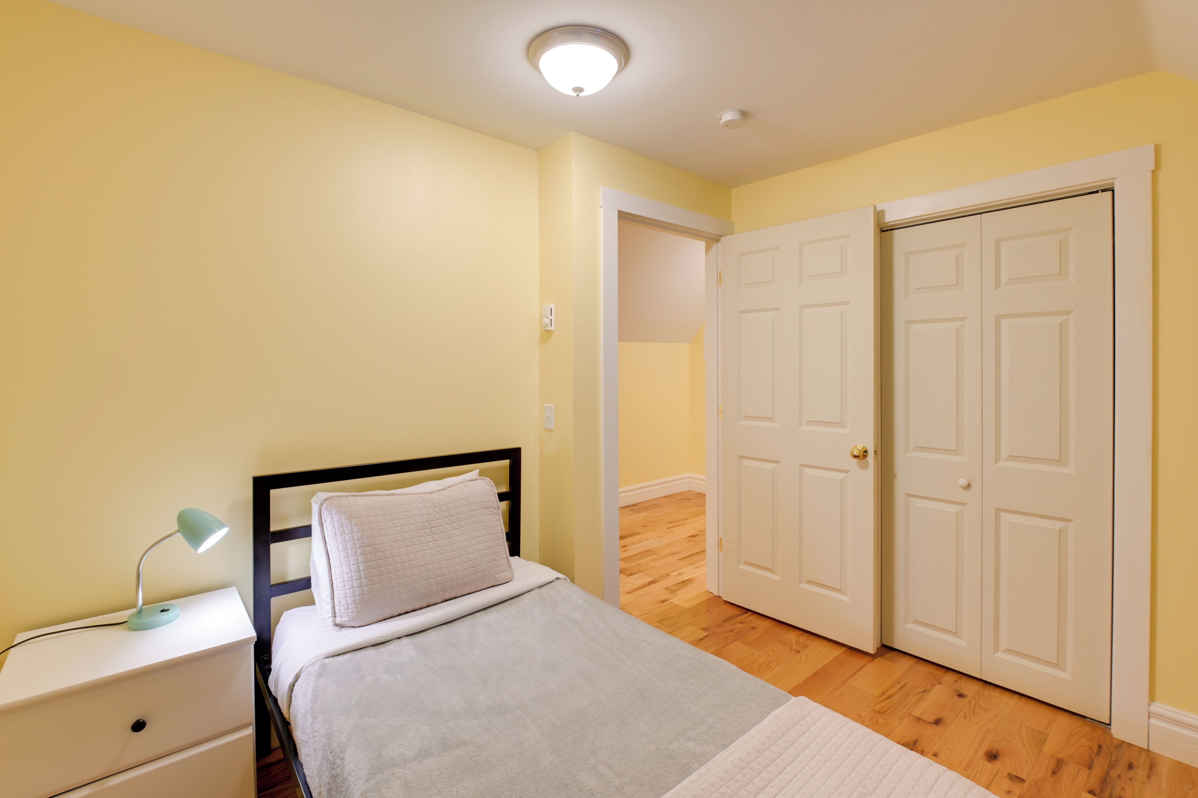 A bedroom with a bed, nightstand, lamp, and two doors.