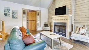 A living room with a sofa, armchairs, a coffee table, a fireplace, and a television mounted on the wall. - Spacious Cabin w/ Views, Near Lake Lawtonka! (Medicine Park)