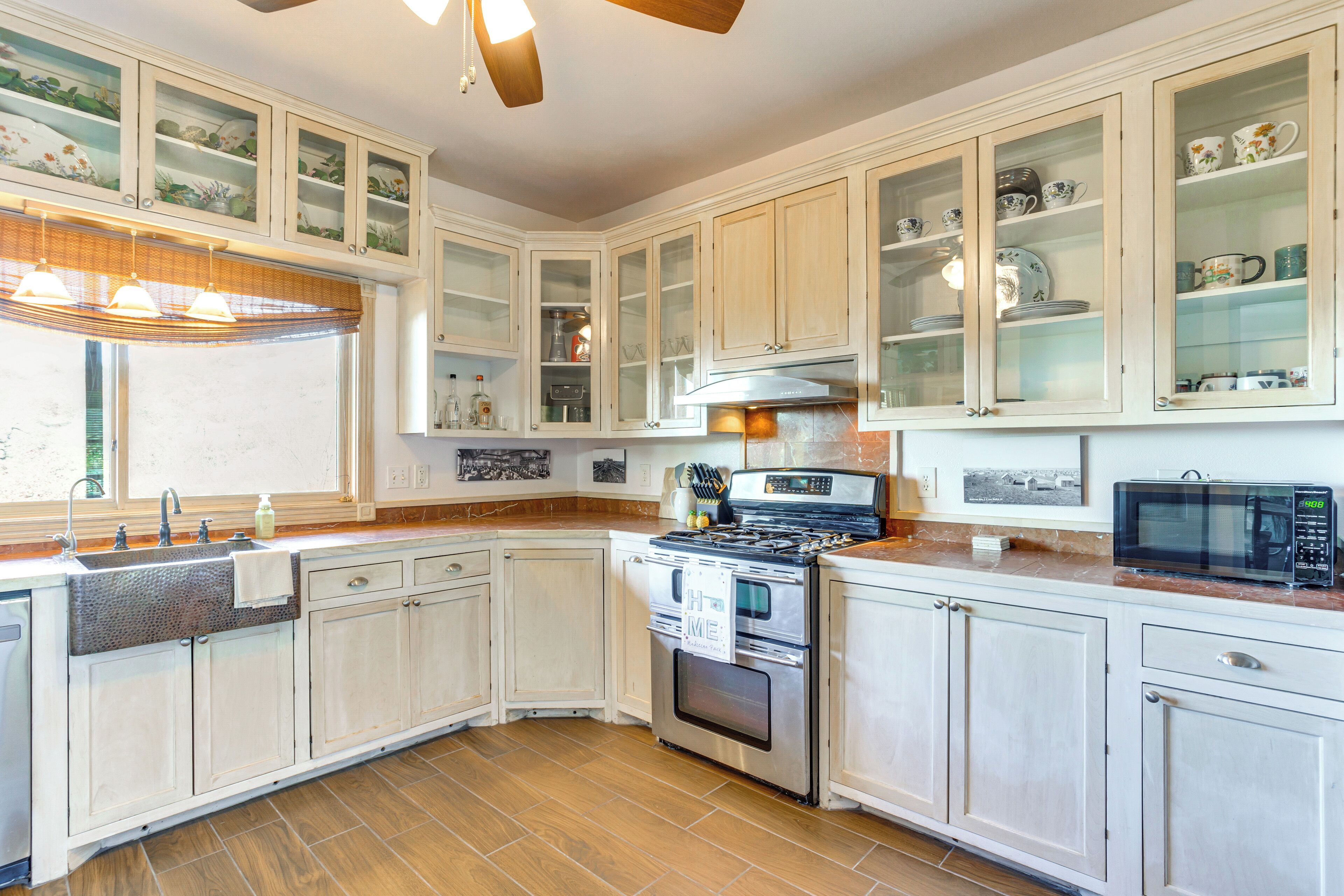 A kitchen with white cabinets, a stove, a microwave, and a window with blinds.