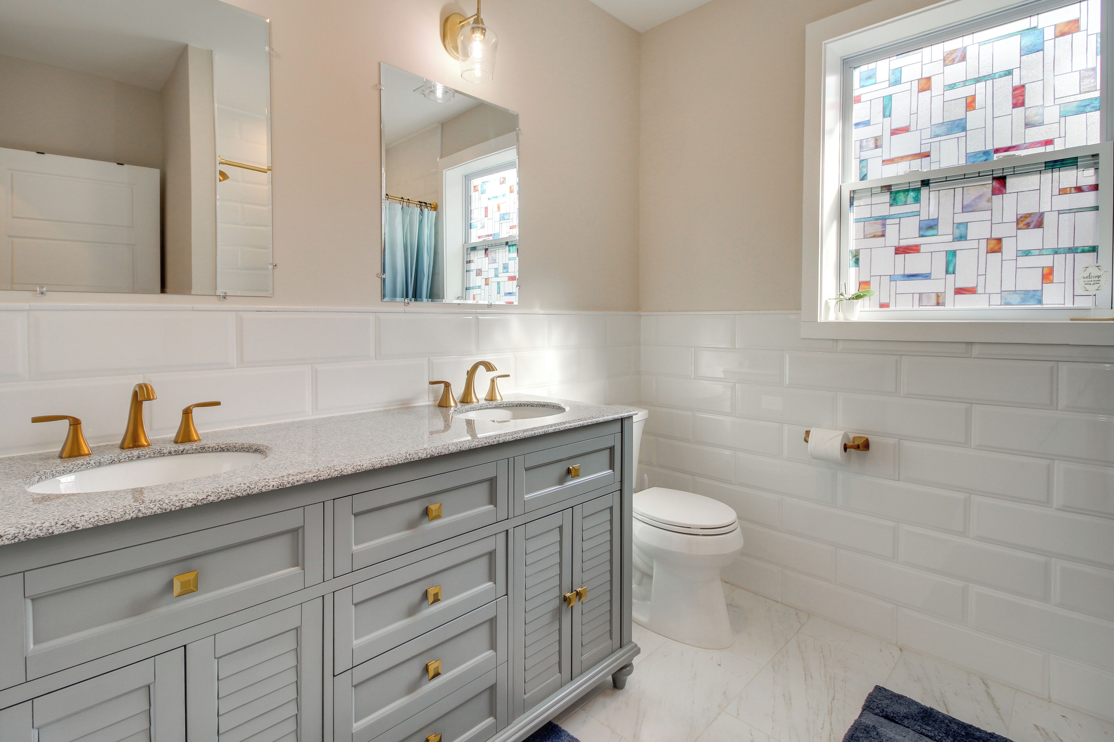 A bathroom with a double sink vanity, a toilet, and a window with a stained glass design.