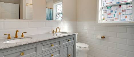A bathroom with a double sink vanity, a toilet, and a window with a stained glass design.