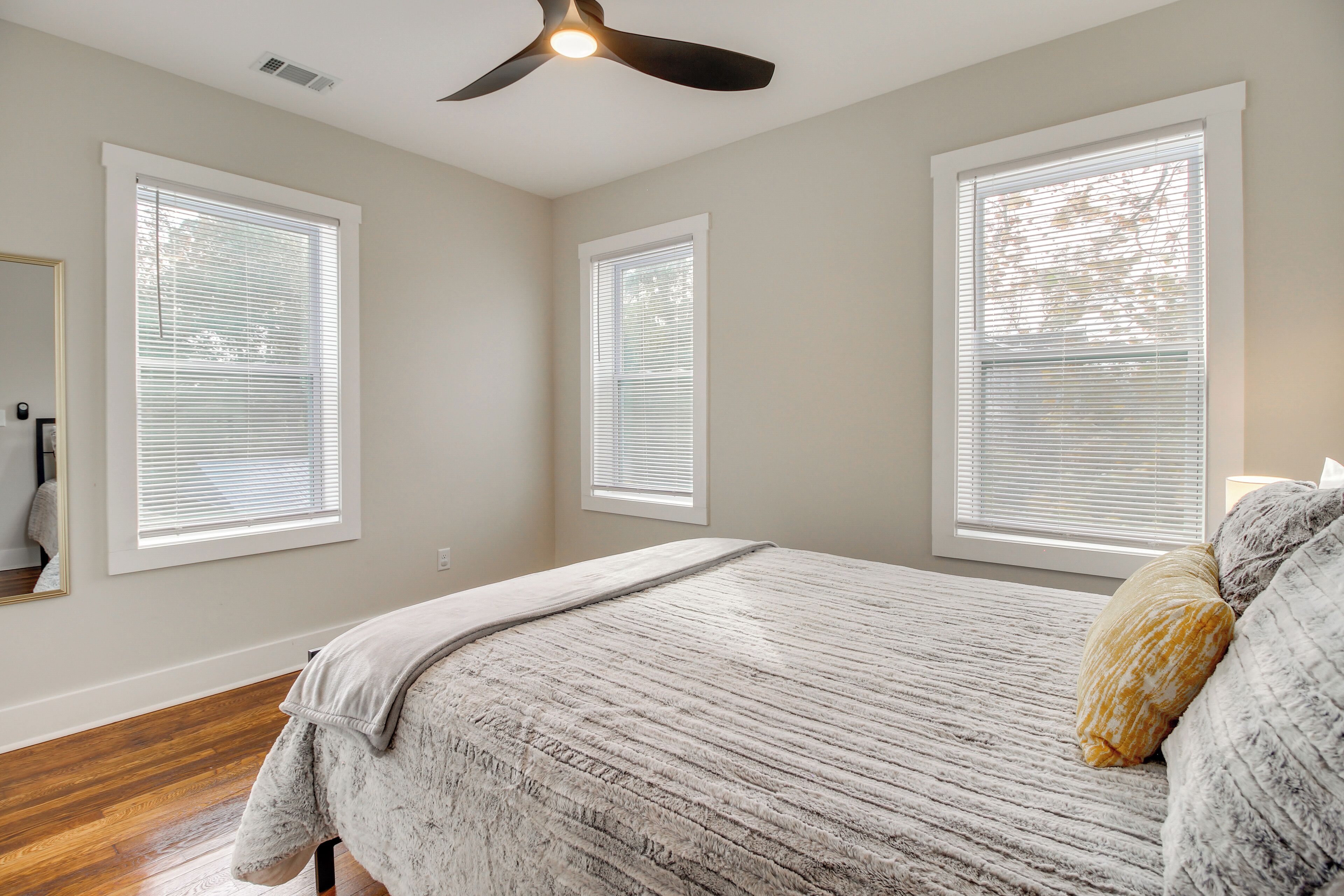 A bedroom with a bed, a ceiling fan, and three windows with blinds.