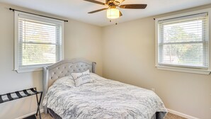 Ein Schlafzimmer mit einem Bett, einem Deckenventilator und zwei Fenstern mit Jalousien.