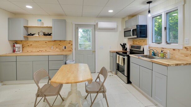 Een moderne keuken met grijze kastjes, een houten aanrecht, een eettafel met stoelen en een raam dat voor natuurlijk licht zorgt.