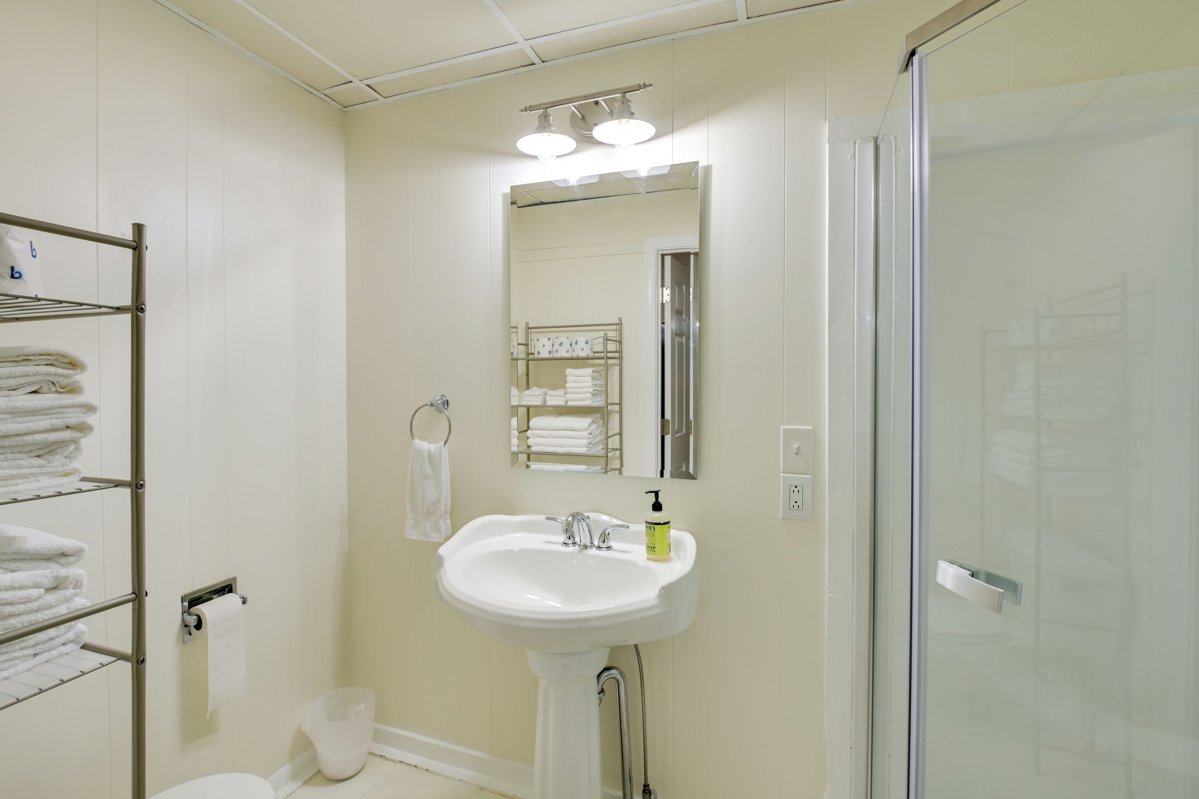 A bathroom with a white sink, a mirror, a glass shower enclosure, and a towel rack with folded towels.