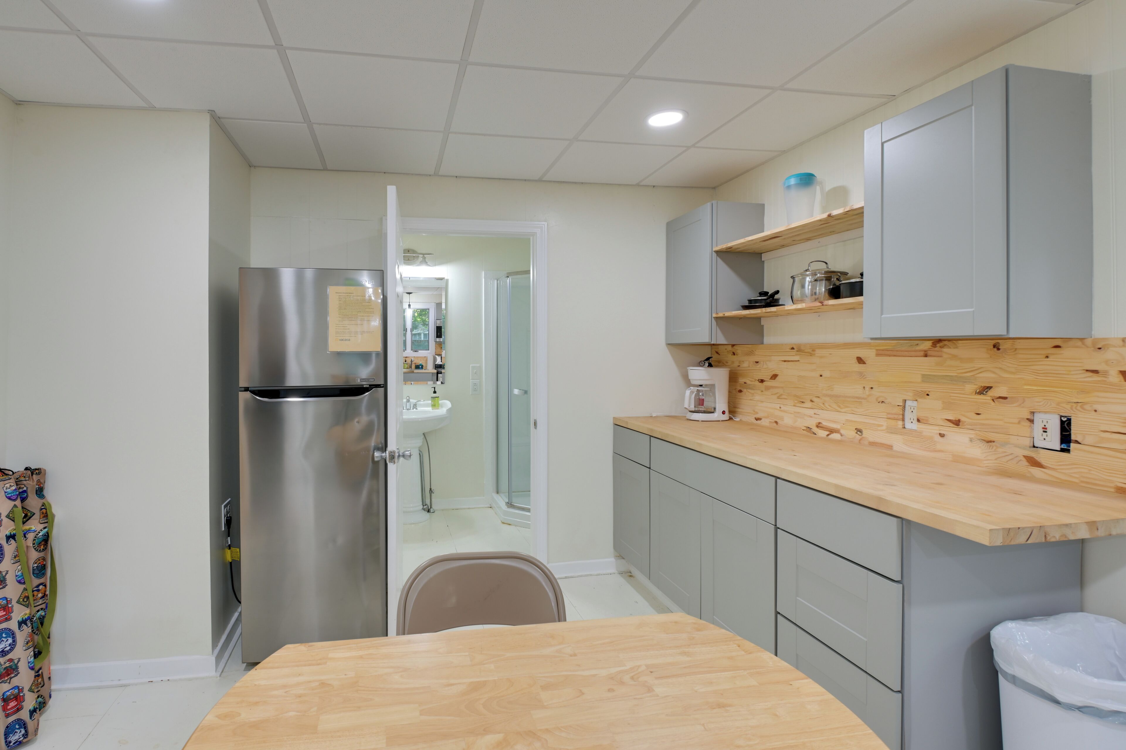 Una cocina con refrigerador de acero inoxidable, encimera de madera, gabinetes grises y un cubo de basura blanco.