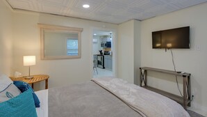 Hotelkamer met een bed, een nachtkastje met een lamp, een aan de muur bevestigde televisie en uitzicht op de keuken door een open deur.