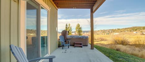 A covered patio with a hot tub, two Adirondack chairs, and a view of a rural landscape.