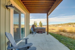 Un porche cubierto con un jacuzzi, dos sillas Adirondack y vistas a un paisaje rural.
