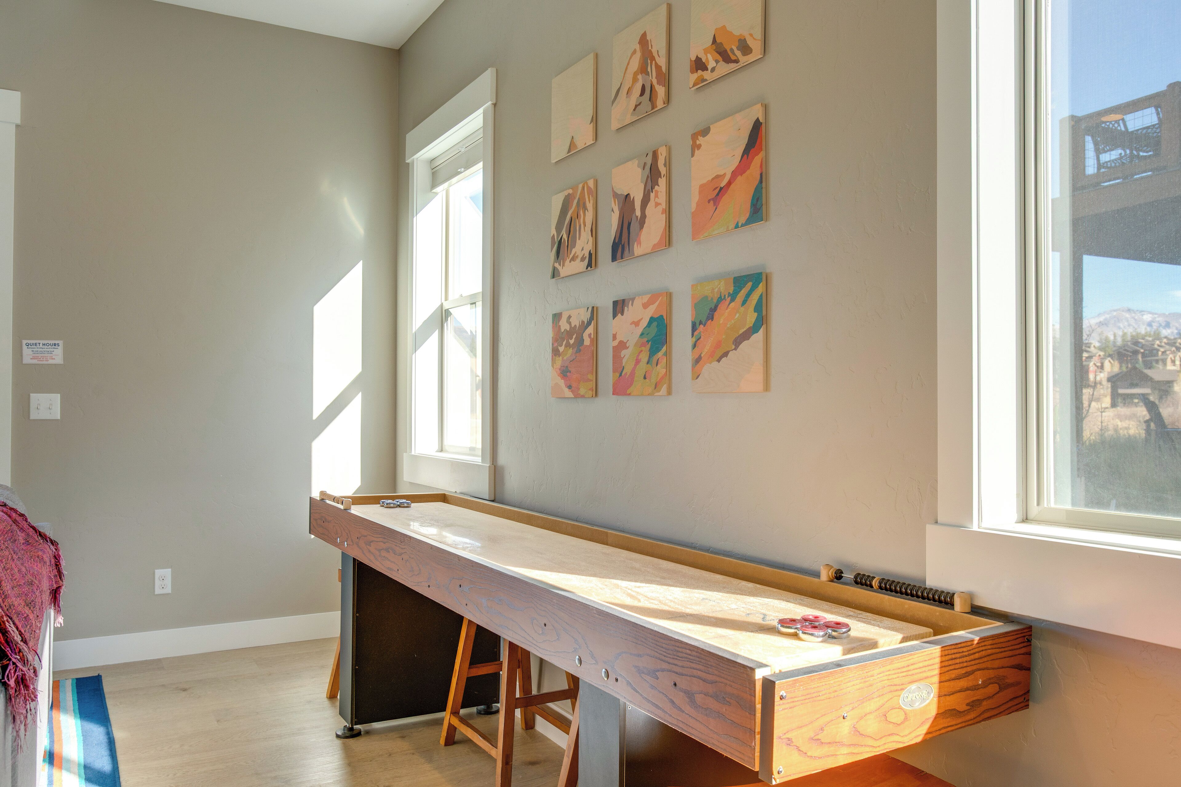A room with a long wooden table, a window with a view of mountains, and several abstract paintings on the wall.