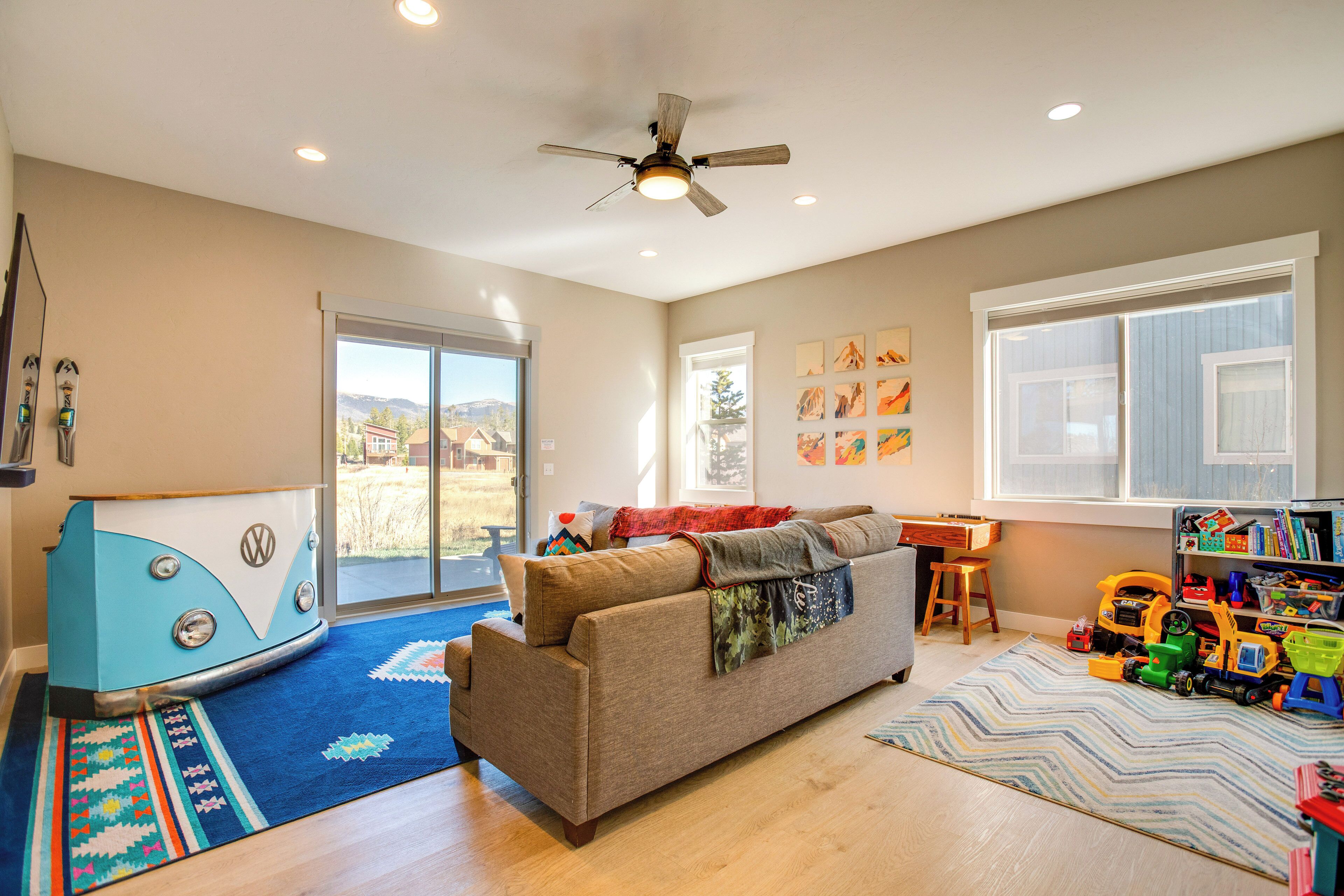 A living room with a sofa, a ceiling fan, a bookshelf, and a window with a view.