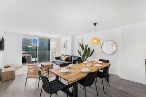 Una sala de estar moderna con comedor, un sofá, una mesa de centro y vistas a la ciudad a través de amplias ventanas.