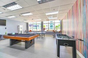 A recreational area with pool tables and foosball tables, large windows, and a view of buildings outside.
