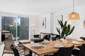 A modern dining area with a wooden table set for four, a black leather sofa, and a view of a cityscape through a large window. - Modern 1BR | Free Parking | Pool | Gym (Brickell)