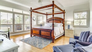 A spacious bedroom with a four-poster bed, large windows, a ceiling fan, and a blue patterned rug. - Pool, Fire Pit & Tennis Court: Gem in Bay St Louis (Bay St Louis)