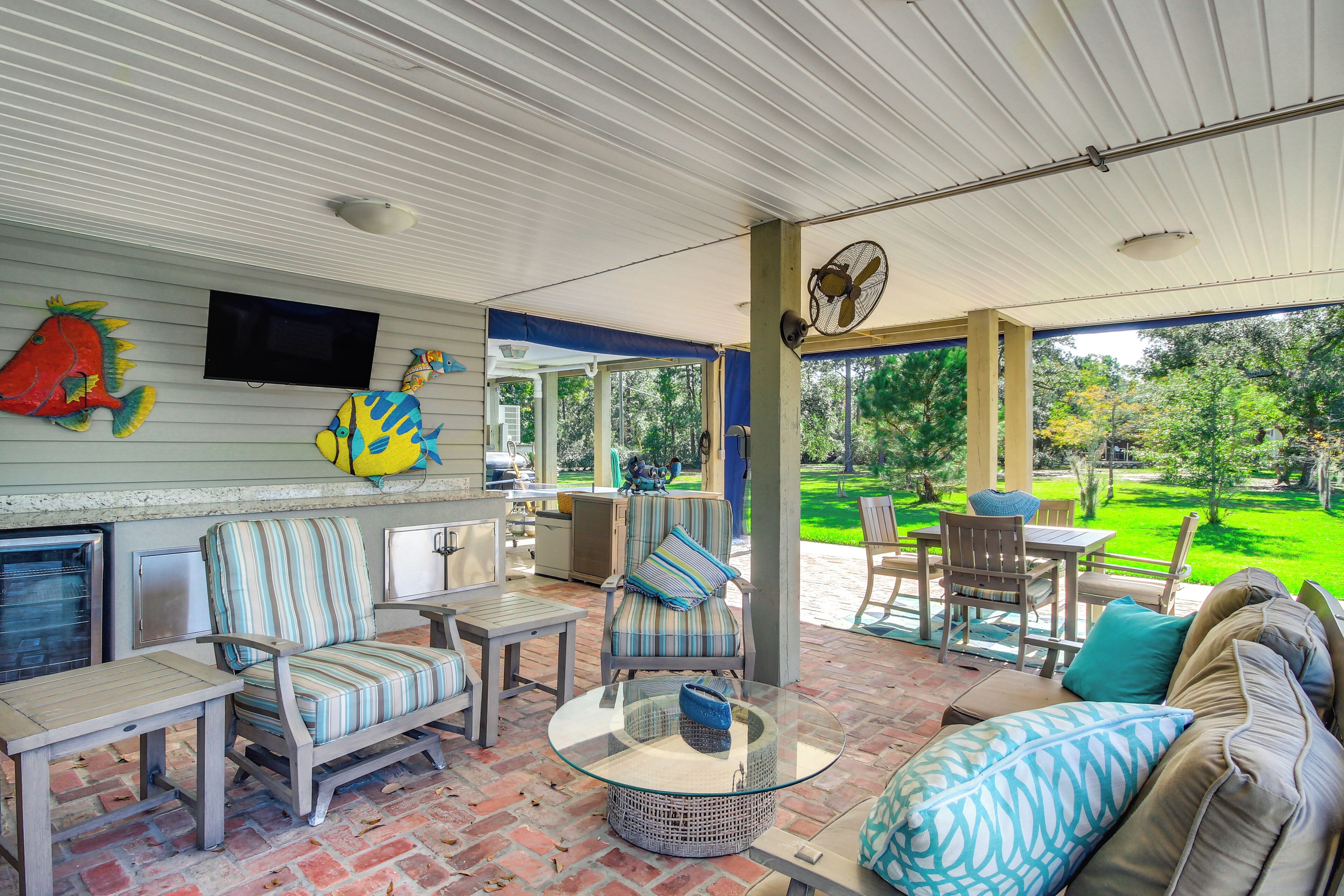 Un patio couvert aménagé avec du mobilier d’extérieur, un téléviseur fixé au mur et une vue sur le jardin.
