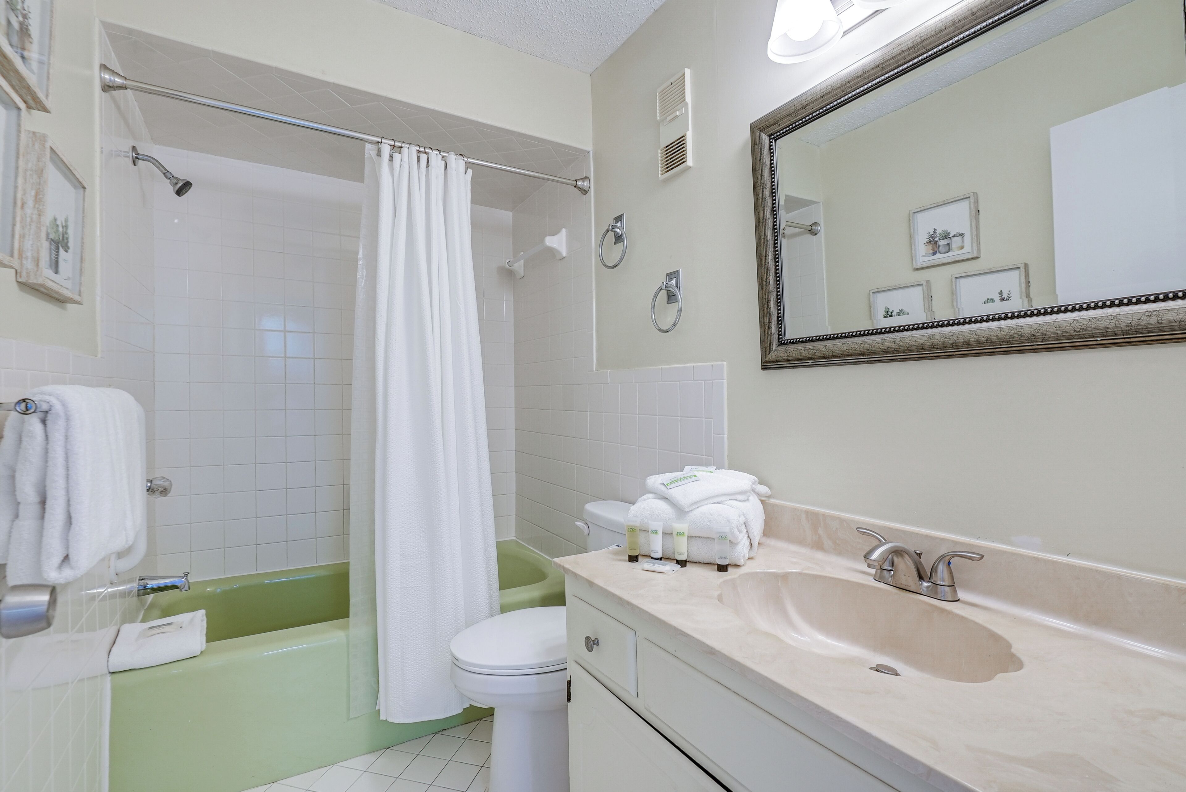 Un baño con una bañera verde, inodoro blanco y lavamanos color beige.