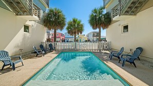 A swimming pool with lounge chairs, a white picket fence, and palm trees. - Rooftop Terrace, Panoramic Deck, Pool & Near Beach (Port Aransas)