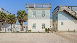 A two-story building with a white and light blue exterior, a wooden fence, and palm trees. - Rooftop Terrace, Panoramic Deck, Pool & Near Beach (Port Aransas)