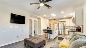 A modern living room with a gray sectional sofa, a tufted ottoman, and a ceiling fan.