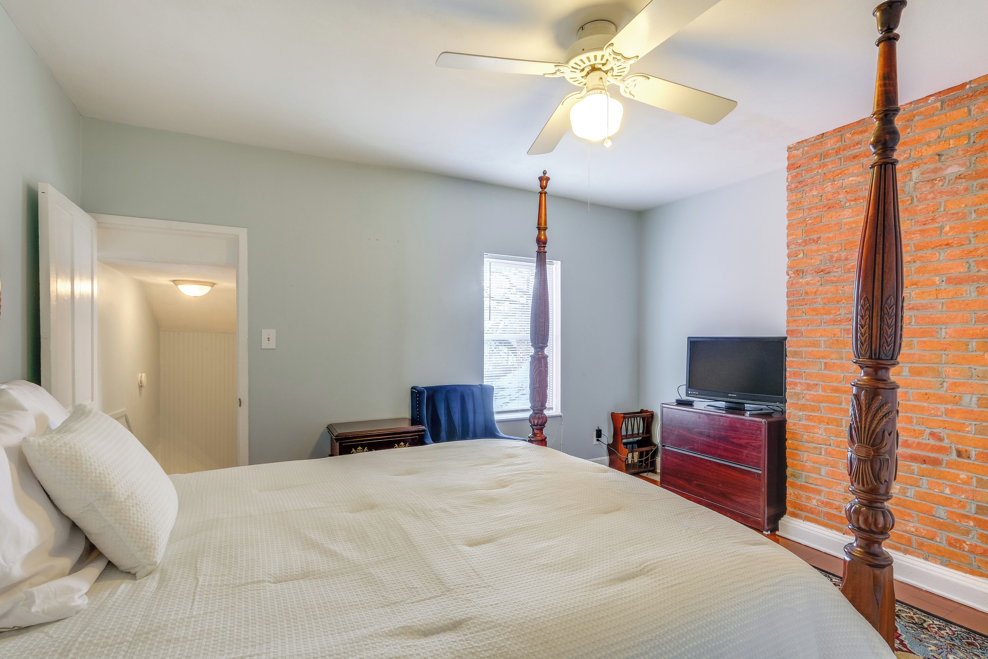 A bedroom with a large bed, a ceiling fan, a brick wall, a television, and a dresser.