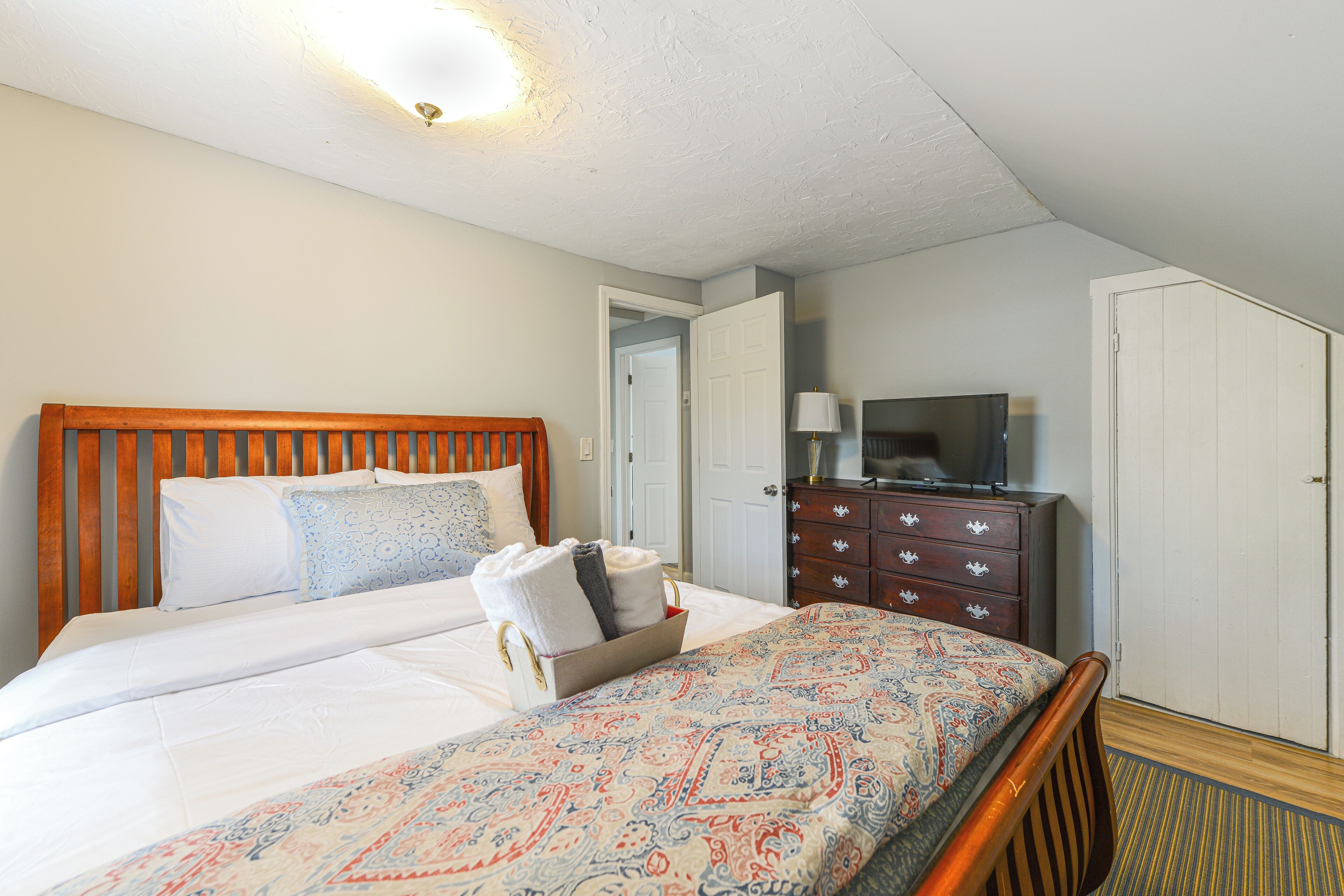 Une chambre d’hôtel avec un grand lit, une commode, une télévision et une porte donnant sur une autre pièce.