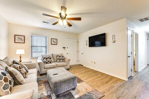 A living room with a ceiling fan, a sofa set, a coffee table, and a flat-screen TV mounted on the wall. - Deck & Fenced Yard: Family Home in Winterville (Winterville)