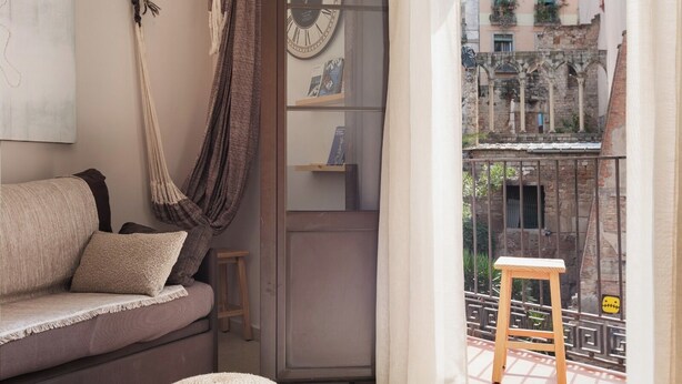 A cozy room with a sofa, macrame wall hanging, a clock, and a view of a historic building.