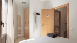 A bedroom with a bed, a wooden wardrobe, a towel rack, and a door leading to a bathroom.