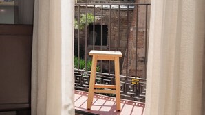 A balcony with a wooden stool, a metal railing, and a view of a building with arched windows and balconies.