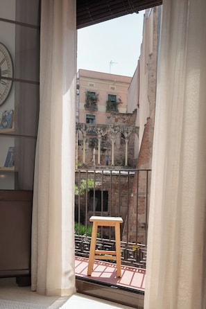 A balcony with a wooden stool, a metal railing, and a view of a building with arched windows and balconies.