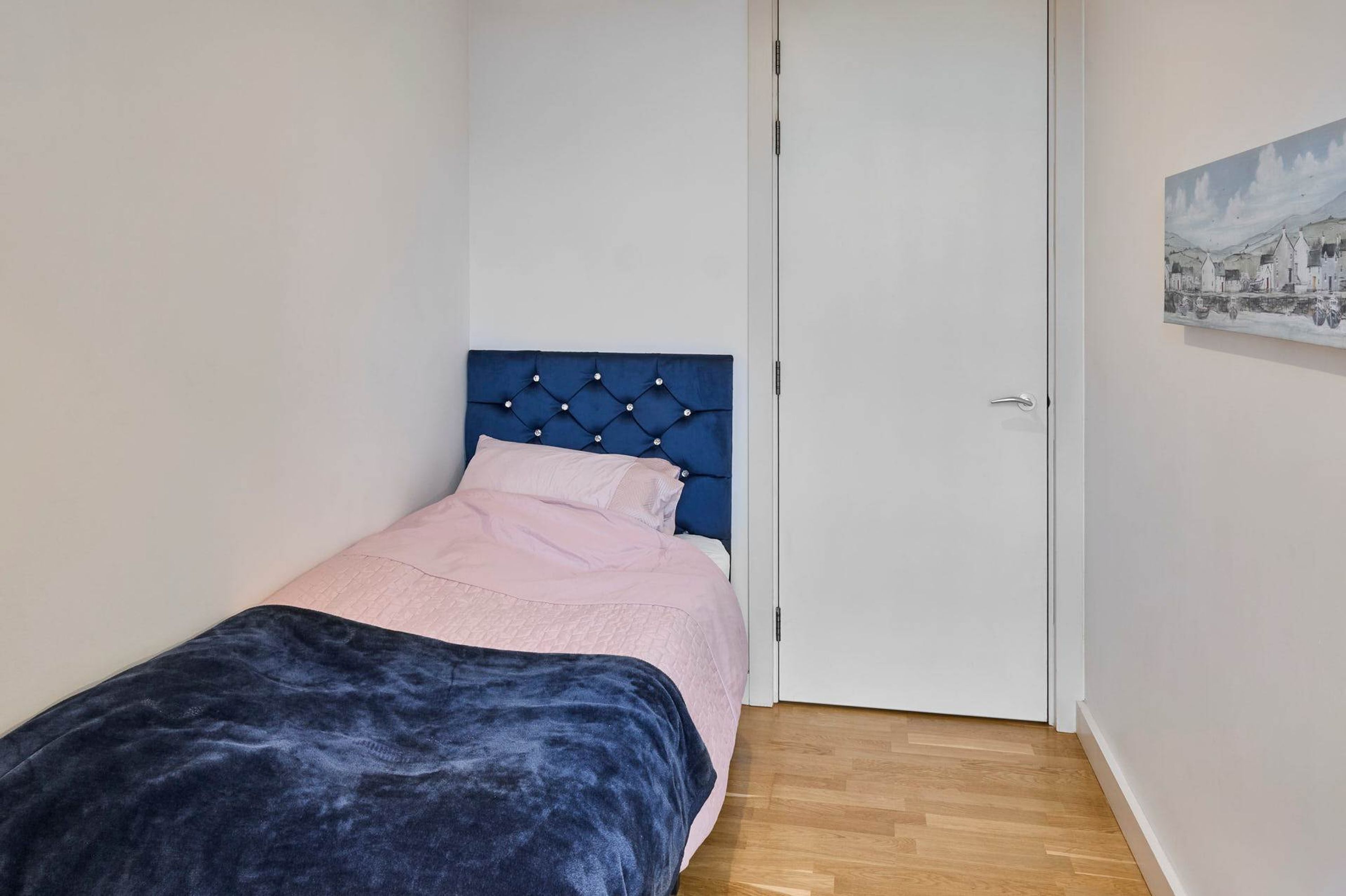A bedroom with a bed, a white door, and a painting on the wall.