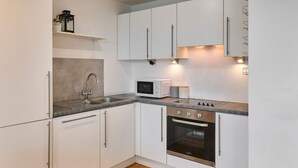 A modern kitchen with white cabinets, a stainless steel sink, a microwave, and an oven.
