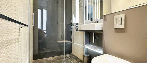 Een moderne badkamer met een douchecabine van glas, een wit toilet en een wastafel met een spiegel erboven.