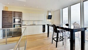 Una cocina moderna con armarios blancos, encimera negra y un comedor con sillas transparentes y una mesa negra.