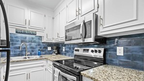 A kitchen with white cabinets, a stainless steel oven, a microwave, and a granite countertop. - Coastal Vista, Steps to Beach/Pool (By Beach Star) (Myrtle Beach)