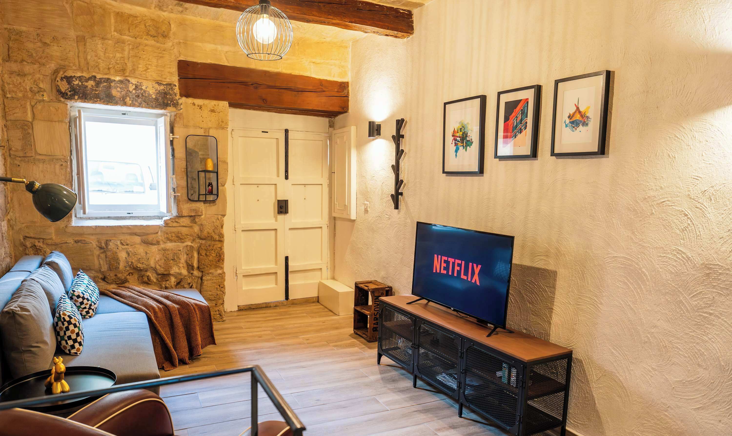 Un salon chaleureux avec un mur en pierre, un plafond en bois, un canapé agrémenté de coussins à motifs, un téléviseur posé sur un meuble en bois et une fenêtre offrant une belle vue.