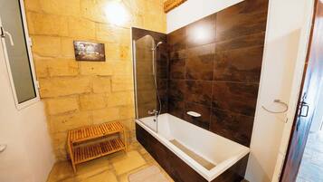 Een badkamer met een stenen muur, een houten bankje, een bad en een douche.