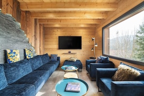 A modern interior with a wooden ceiling, a large flat-screen TV mounted on the wall, and a seating area with blue sofas and a coffee table.