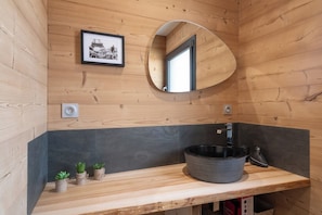 A wooden cabin interior with a round mirror, a framed picture, and a sink with a basin.