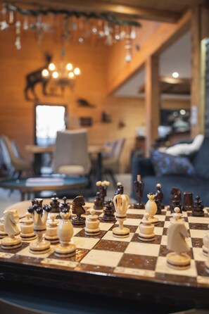 A chessboard with pieces in a room with a wooden wall, a hanging light fixture, and a window.