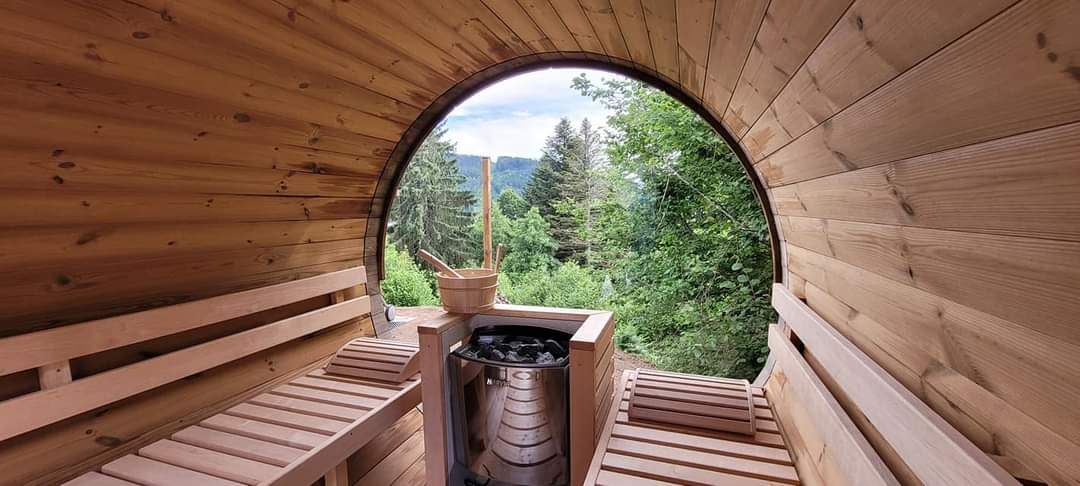 A sauna with wooden benches and a view of a forest through a circular opening.