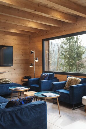 A cozy room with wooden walls, a large window, a blue sofa, and a television.