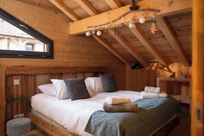 A cozy wooden cabin bedroom with a bed, pillows, a nightstand, and a window.