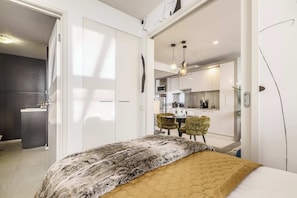 Ein modernes Schlafzimmer mit einem großen Bett, einer Essecke mit Stühlen und einer Küche im Hintergrund.