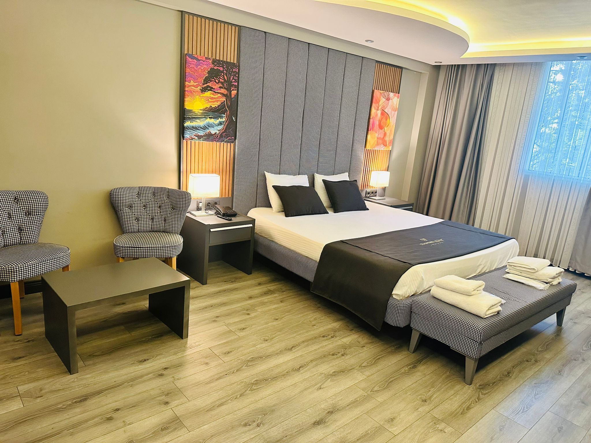 A modern hotel room with a large bed, a desk, two chairs, and a small sofa.